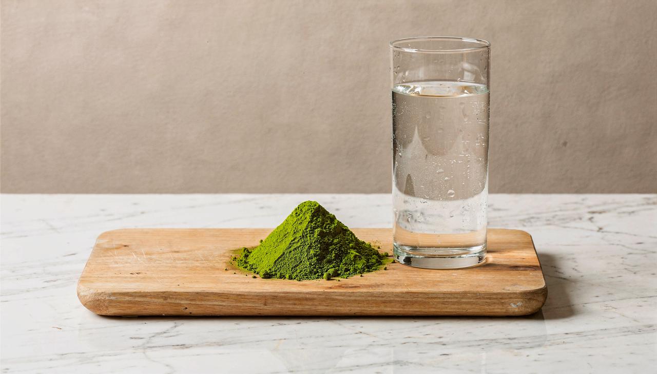 A scoop of green powder beside a glass of water — clinical, minimal