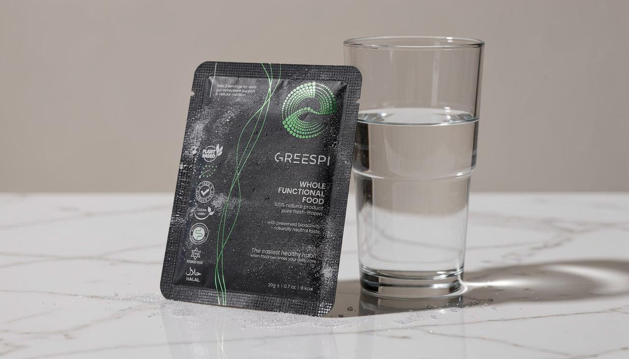 A Greespi sachet standing next to a glass of water on a marble counter